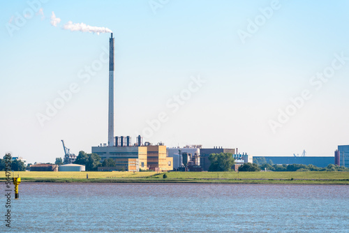 View of a riverside chemical factory with a tall smokestack belching out white smoke at sunset