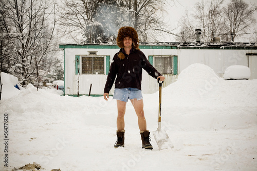 A portrait of a young man wearing a large, furry hat and jean shorts while holding a shovel. photo