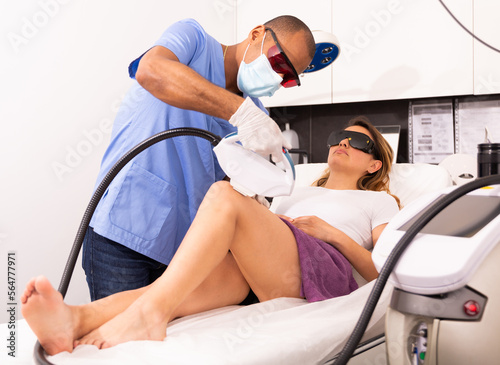 Portrait of qualified Latin American cosmetologist and female client during laser hair removal procedure in aesthetic cosmetology office