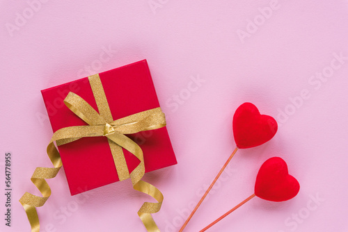 Fototapeta Naklejka Na Ścianę i Meble -  Gift in a red box with golden bow and two toy hearts on pink background. Valentines day concept. Top view, flat lay
