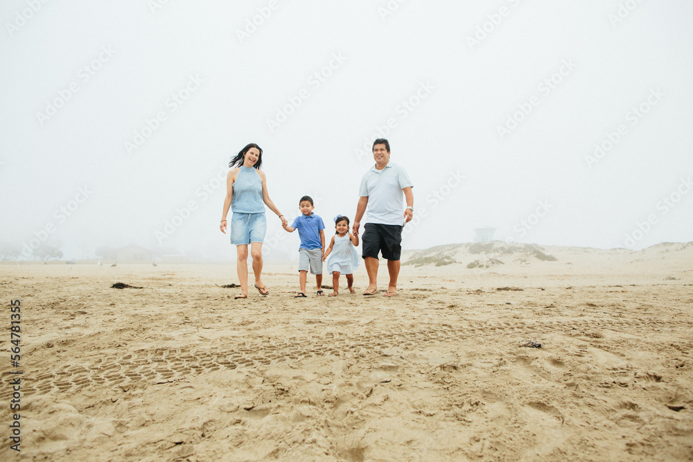 Family Of Four Walks Together Holding Hands At Beach Family Of Four Walks Together Holding Hands At Beach