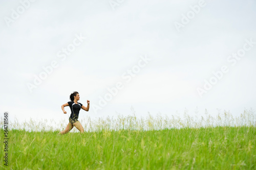 Young woman running on grass trail through a bright green field at Spirit Mound, South Dakota. photo
