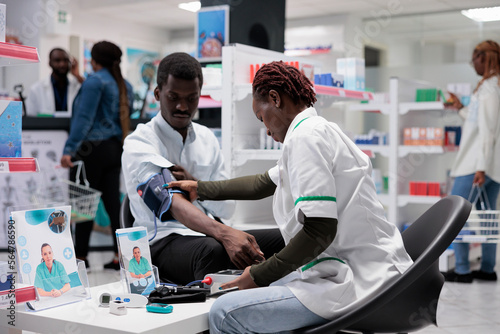 Pharmacist consultation, medic measuring patient blood pressure. Woman examining african american man health in drugstore, cardiovascular disease diagnostic, medical check up