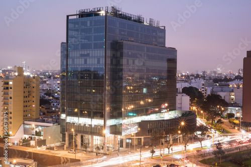 mirrored modern building of a corporation with a highway with a lot of traffic and the line of the metropolitan bus at night, oct 2020 miaflores lima peru