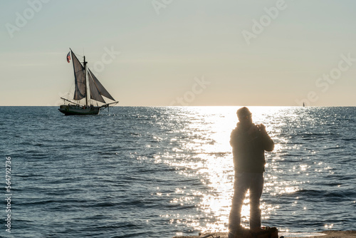 A fisherman is silhouetted against the glare of the late day sun as he prepares his line from a pier on Lake Michigan.