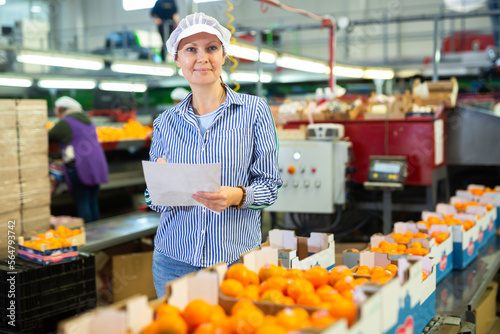 Diligent female worker takes inventory of ripe tangerines on a packing line.