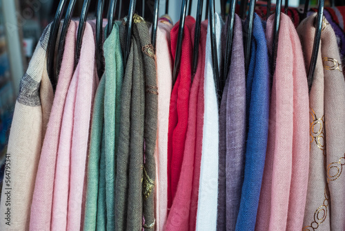 Clothes color on a rack. Row of different colorful womens textiles on a hanger. A lot of scarfs of different colors