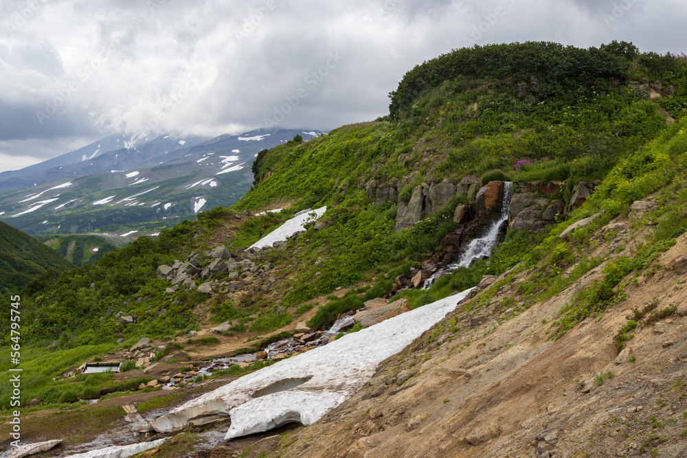 Summer mountain landscape. A small waterfall and a stream among the rocks on the mountainside. Travel on the Kamchatka Peninsula. Beautiful nature of the Russian Far East. Kamchatka Territory, Russia.
