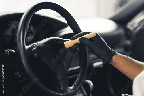Close-up shot of unrecognisable man wearing black gloves inside car brushing the steering wheel. Precision work. Car interior detailing concept. Horizontal indoor shot. High quality photo