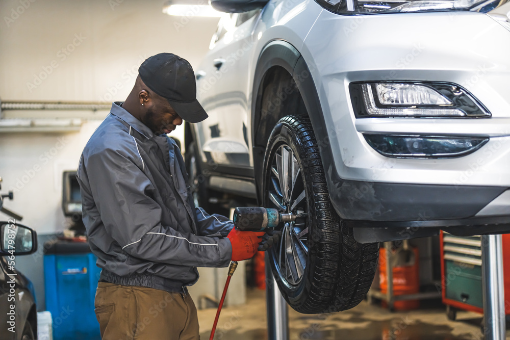 Medium shot of a black mechanic screwing a car wheel with an impact wrench. Repair shop concept. High quality photo Medium shot of a black mechanic screwing a car wheel with an impact wrench. Repair shop concept. High quality photo