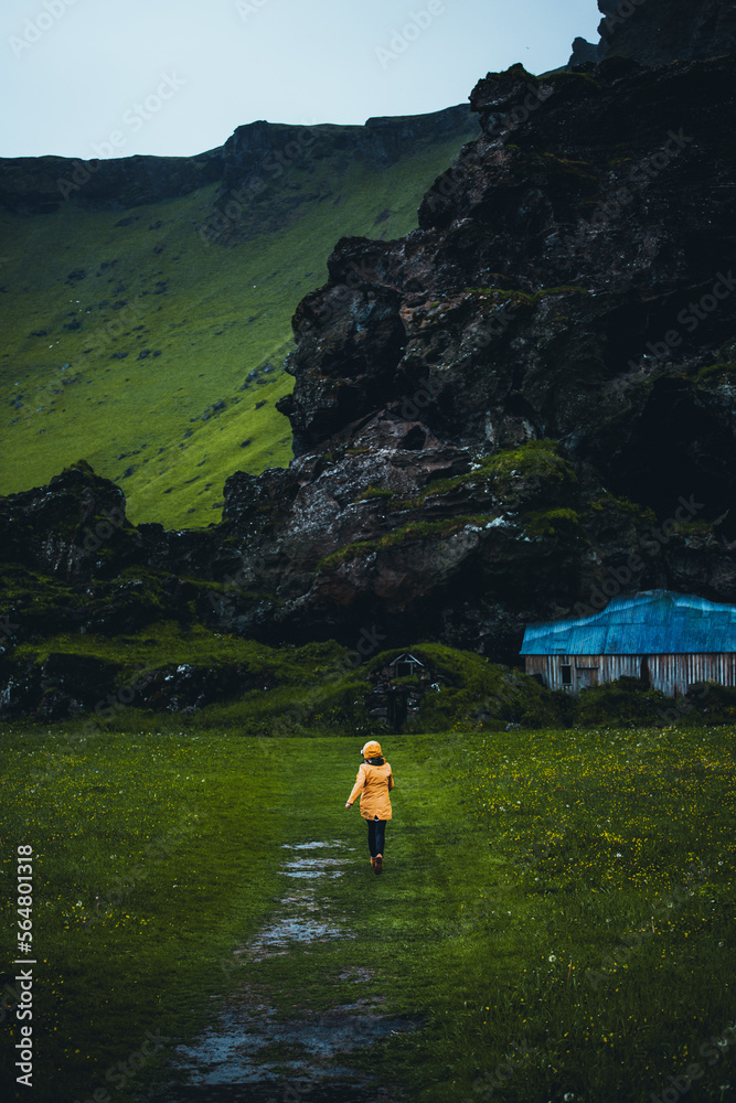 Skogar, Iceland: girl walking to the monolithic rock with traditional houses and barns built in of against it