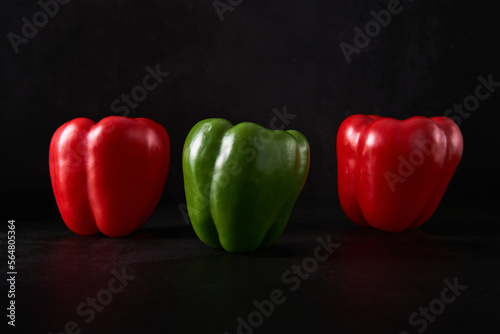 A green pepper in the foreground and two red parika in the background. Foreground and background are in black pattern. Also suitable for ripe vs unripe concepts.  © Francesco
