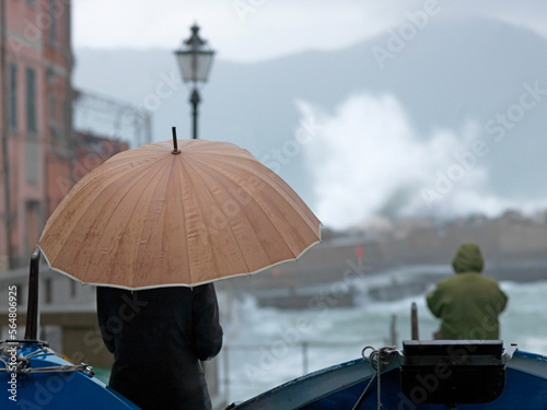 Woman with umbrella wathes storm waves crash into village photo