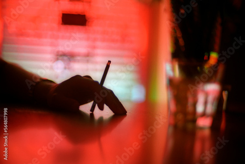 A hand holds a cigarette in a dimly lit bar. photo