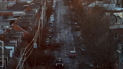 Aerial long zoom of urban city street with barren trees during winter dusk. Row houses line street in tight shot. Reveal of bright sunset. photo