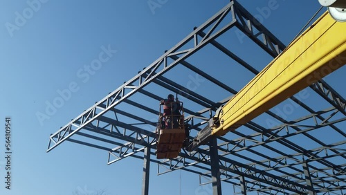 Workers on aerial work platforms build the metal structure of the roof of a large building