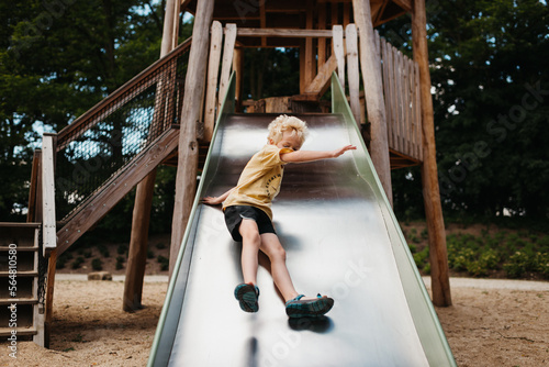 Blond toddler going down a slide at the playground photo
