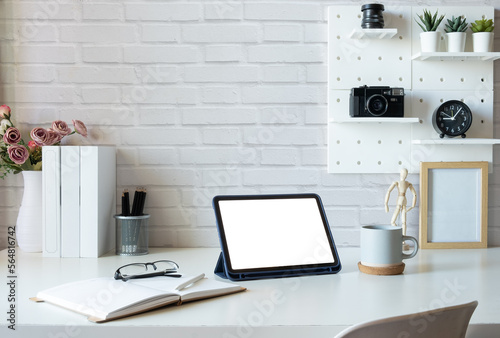 Creative workspace with digital tablet, books, coffee cup and stationery on white desk.