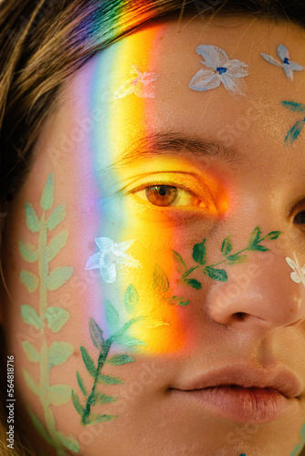 Closeup woman face with painted flowers and rainbow light photo