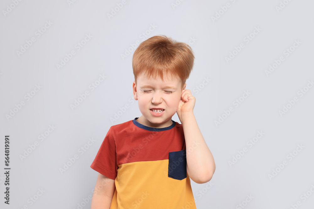 Little boy suffering from ear pain on light grey background
