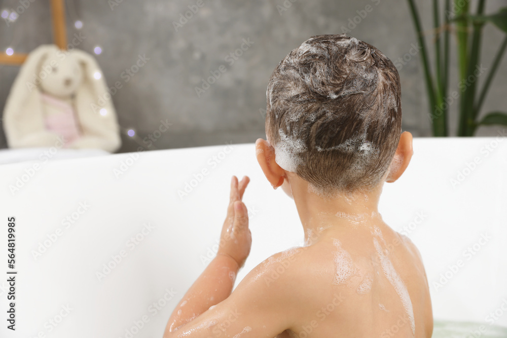 Cute little boy washing hair with shampoo in bathroom, back view Cute little boy washing hair with shampoo in bathroom, back view