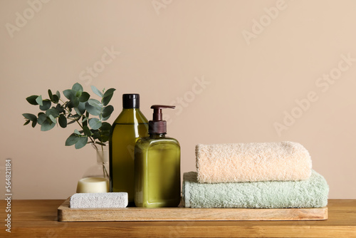 Solid shampoo bar and bottles of cosmetic product on wooden table near beige wall
