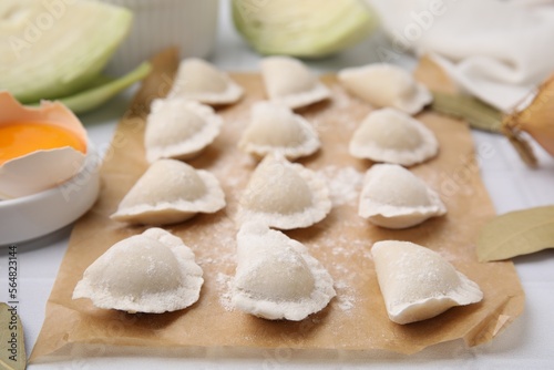 Raw dumplings (varenyky) with tasty filling and flour on parchment paper, closeup