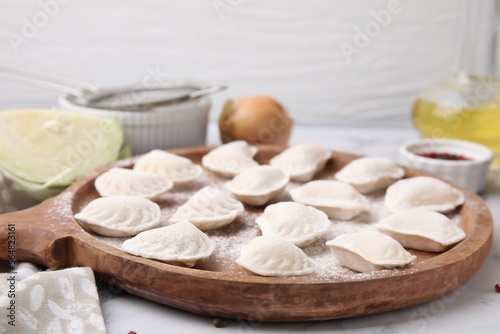 Raw dumplings (varenyky) with tasty filling and flour on wooden board, closeup