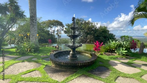 Classic water fountain in a beautiful garden with green water pond,flowers, trees, purple flowers, blue sky, on the horizon the city of Caruaru state of Pernambuco photo