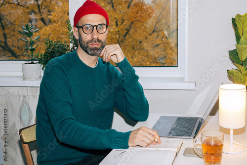 Adult man in a red winter hat at the workplace in his home office. photo