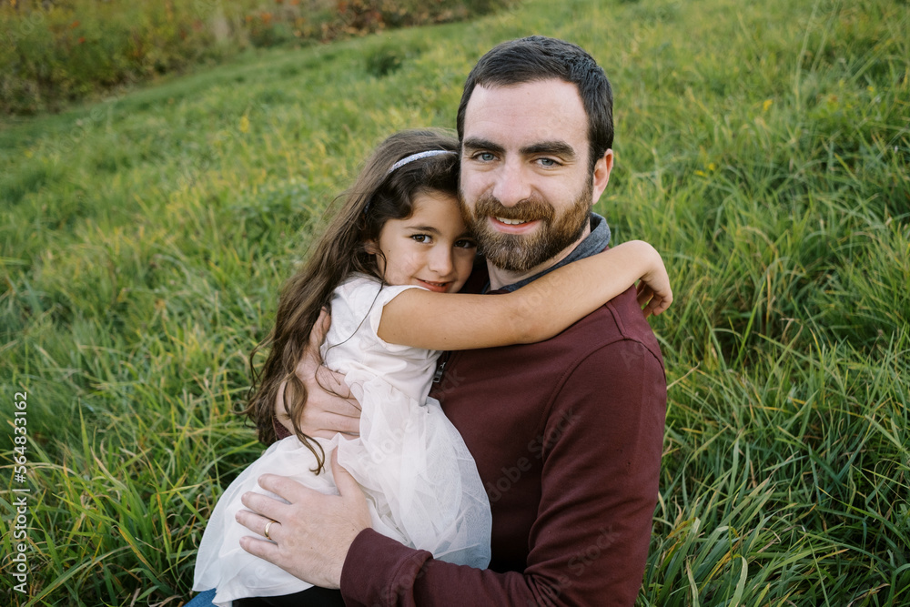smiling father hugging his daughter while sitting down outdoors smiling father hugging his daughter while sitting down outdoors
