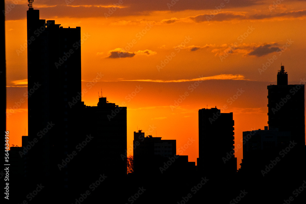 The city, a stone jungle waking up or entering the night lit by a deep orange that marks its silhouette.