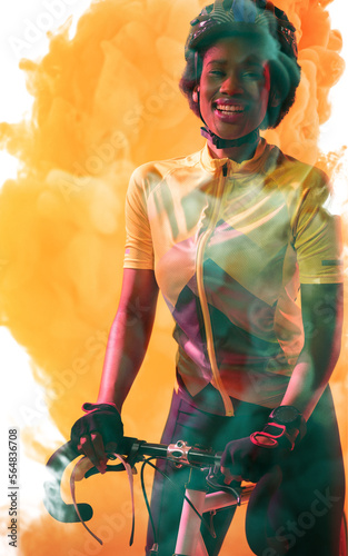 Portrait of african american female athlete wearing helmet standing with bike on smoky background