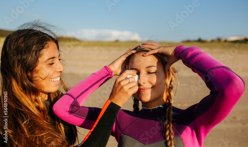 Happy woman helping girlfriend to apply sunscreen