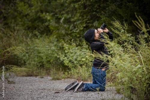 Young boy photographing trees on a gravel trail