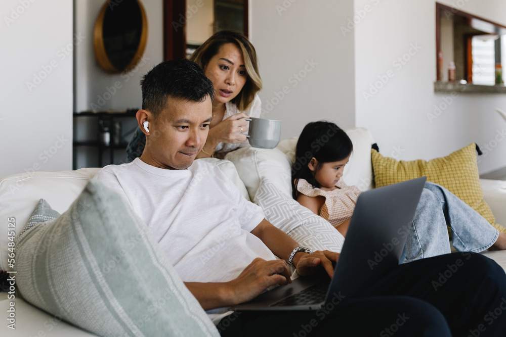 Family of three on the couch in a living room with gadgets Family of three on the couch in a living room with gadgets