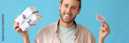Handsome young man with gift card and present on light blue background photo