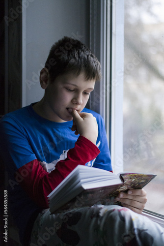 boy reading book with his finger inside mouth photo