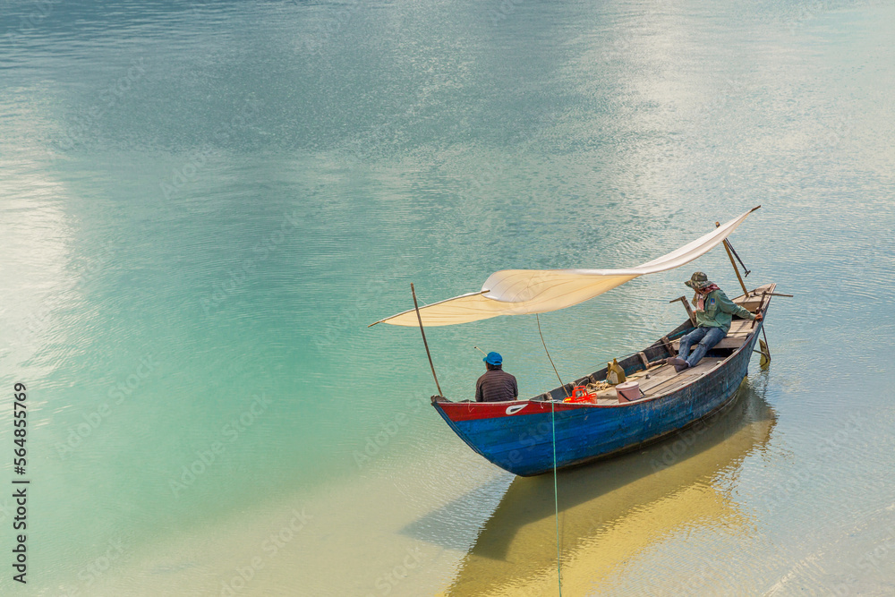 A singe blue fishing boat sitting on a large calm coastal lagoon at Lang Co in Vietnam
