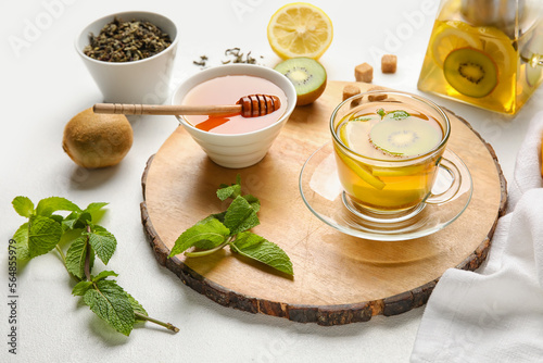 Board with glass cup of fruit tea, kiwi, lemon, mint and honey on white background