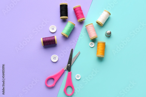 Thread spools, buttons and scissors on color background