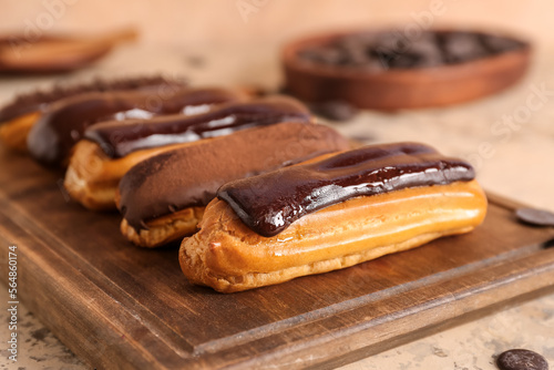 Foto Wooden board with tasty chocolate eclairs on table, closeup