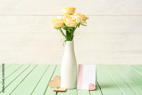 Vase with beautiful rose flowers and blank card on color wooden table © Pixel-Shot