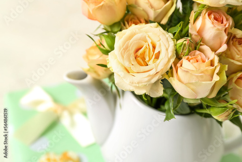 Teapot with beautiful rose flowers on light background, closeup