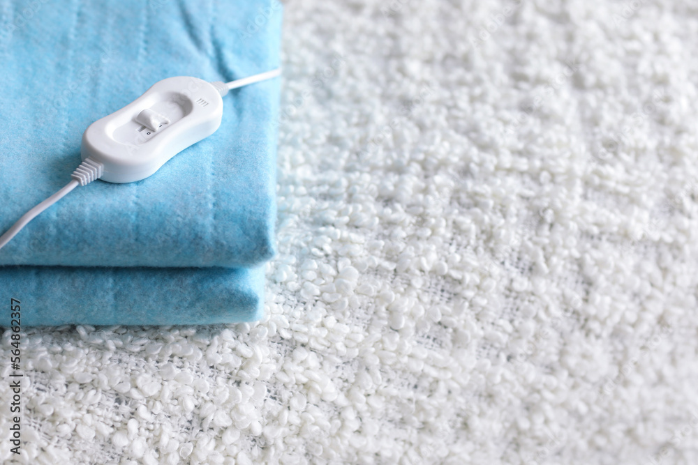 Folded electric heating pad with controller on white blanket in bedroom, closeup Folded electric heating pad with controller on white blanket in bedroom, closeup