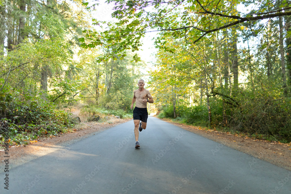 Fit man running hard on road in autumn or fall. Fit man running hard on road in autumn or fall.