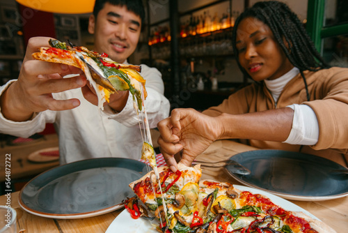 Friends sharing delicious vegetarian pizza in restaurant  photo