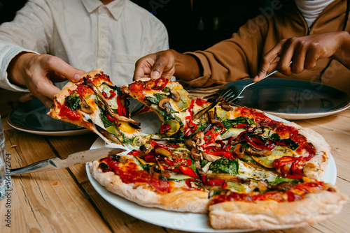 Anonymous Friends sharing delicious vegetarian pizza in restaurant  photo