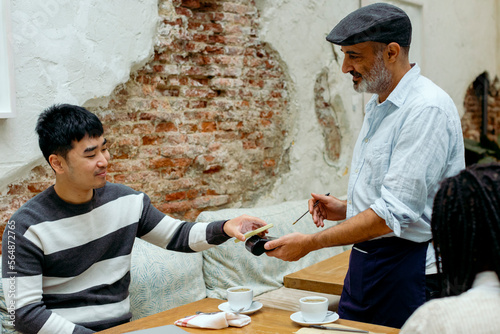 Man in cafe interacting with waiter while paying with mobile phone