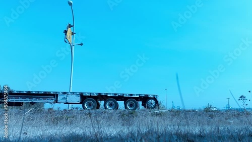 Loop video transport truck red with empty flatbed trailer lowboy six wheeler followed by white sports car and another gray vehicle 4 door sedan on a clear blue day. Easy repeat continuous playback photo